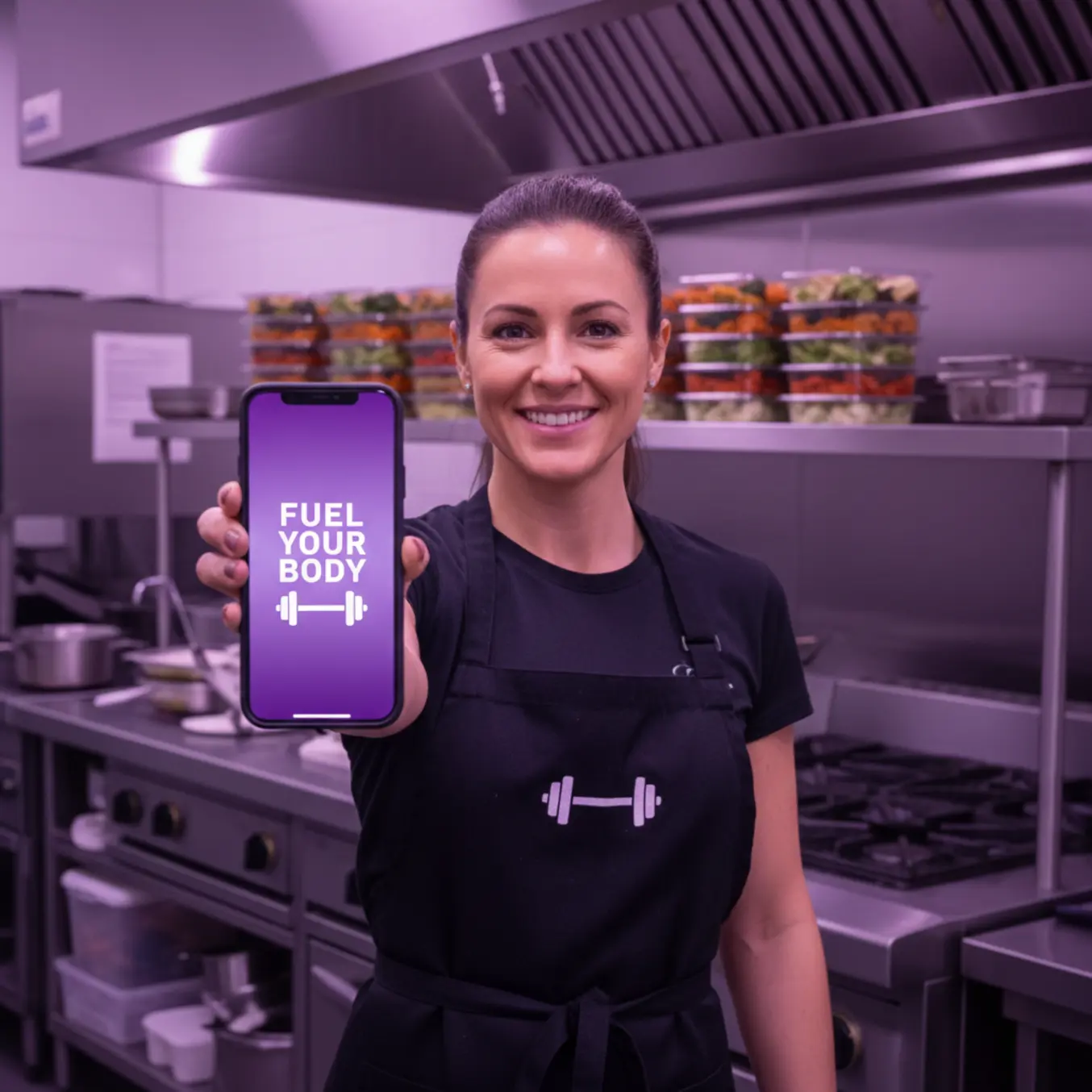 Empreendedor de marmitaria fitness sorrindo com celular na cozinha profissional